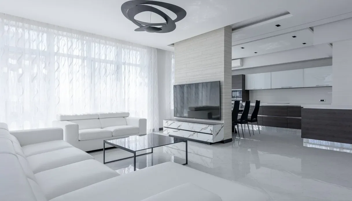 Soggiorno total white con la lampada a sospensione Pirce di Artemide, a spirale in metallo scuro, divani in pelle bianca, tavolino in vetro nero, pavimento lucido effetto marmo e cucina a vista sullo sfondo